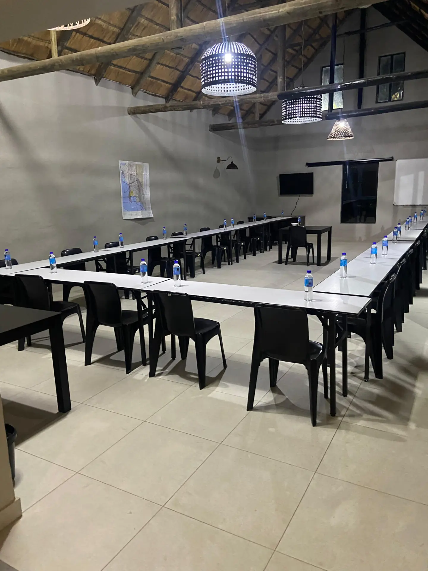 U-shaped conference seating under the thatched roof, set with water and a projector screen