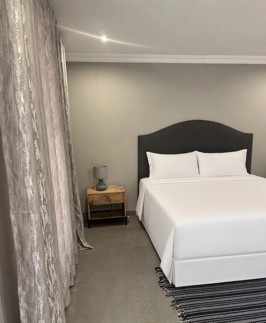 Guest room bedside with wooden nightstand and soft curtains